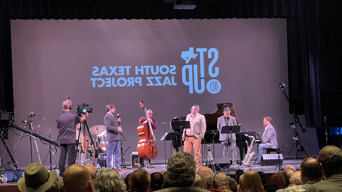 photo of jazz musicians on a stage with playing instruments with an audience looking on 